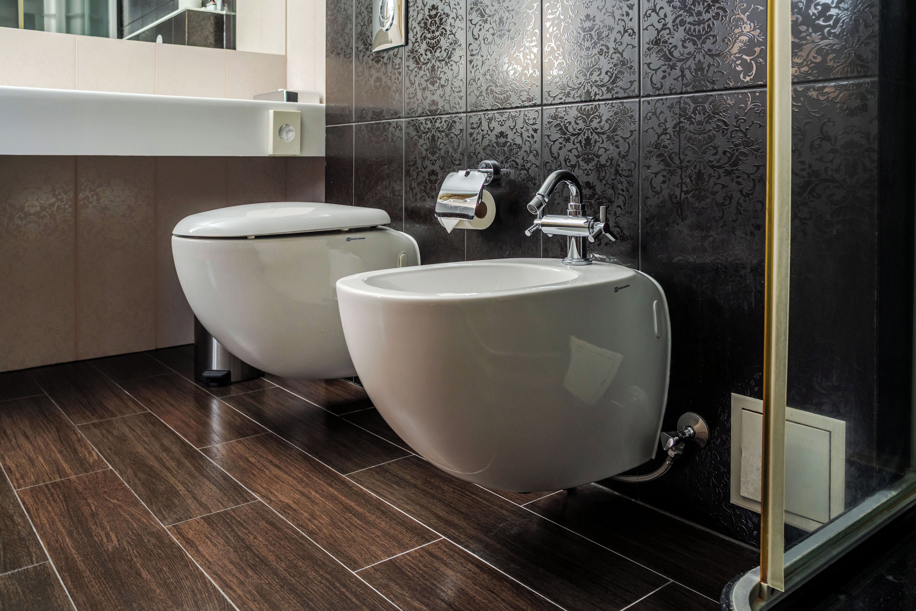 A modern bathroom with two toilets, a sink, and a mirror.