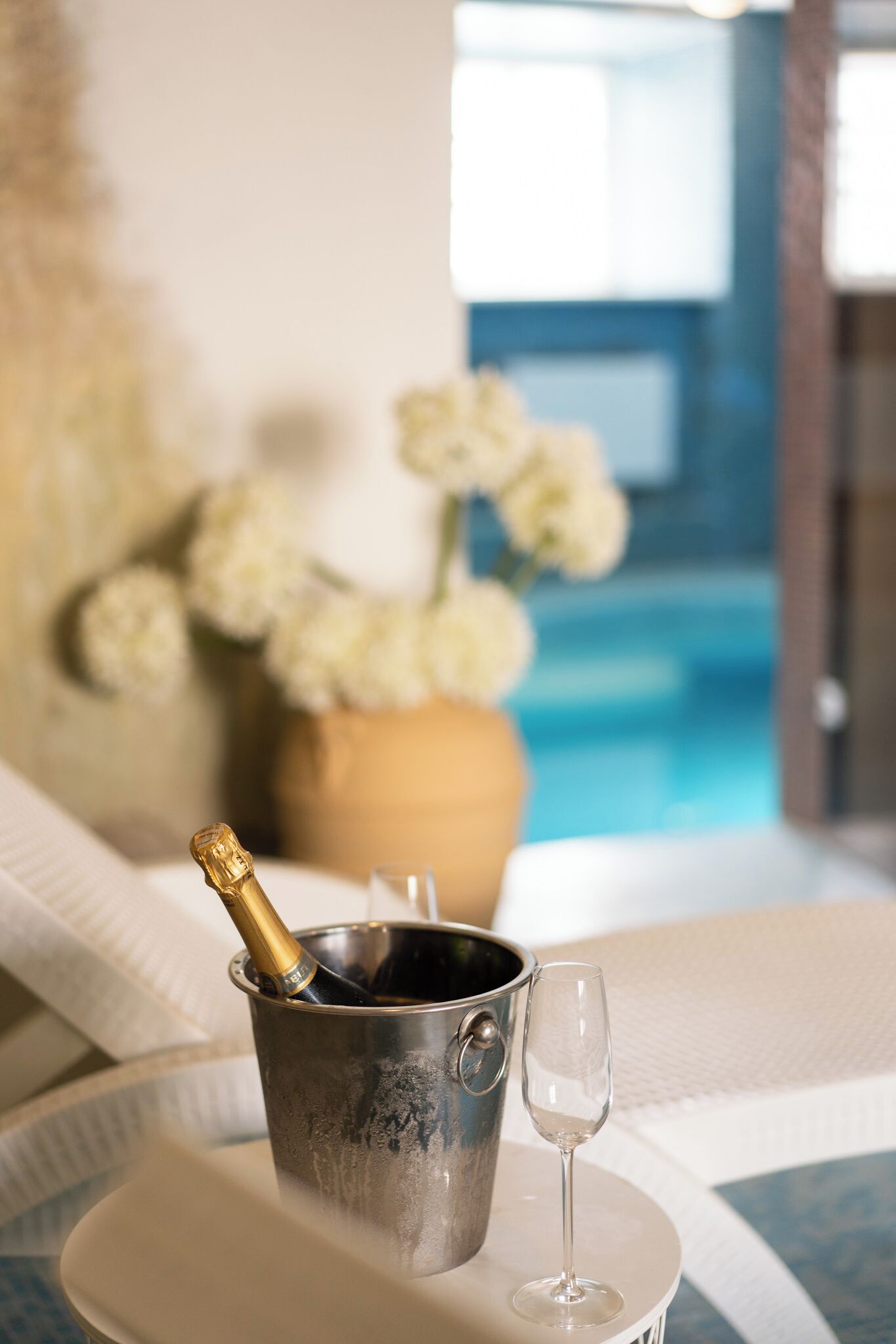Un seau en métal, une bouteille de champagne et un verre, le tout posé sur un plateau blanc, près d’une piscine.