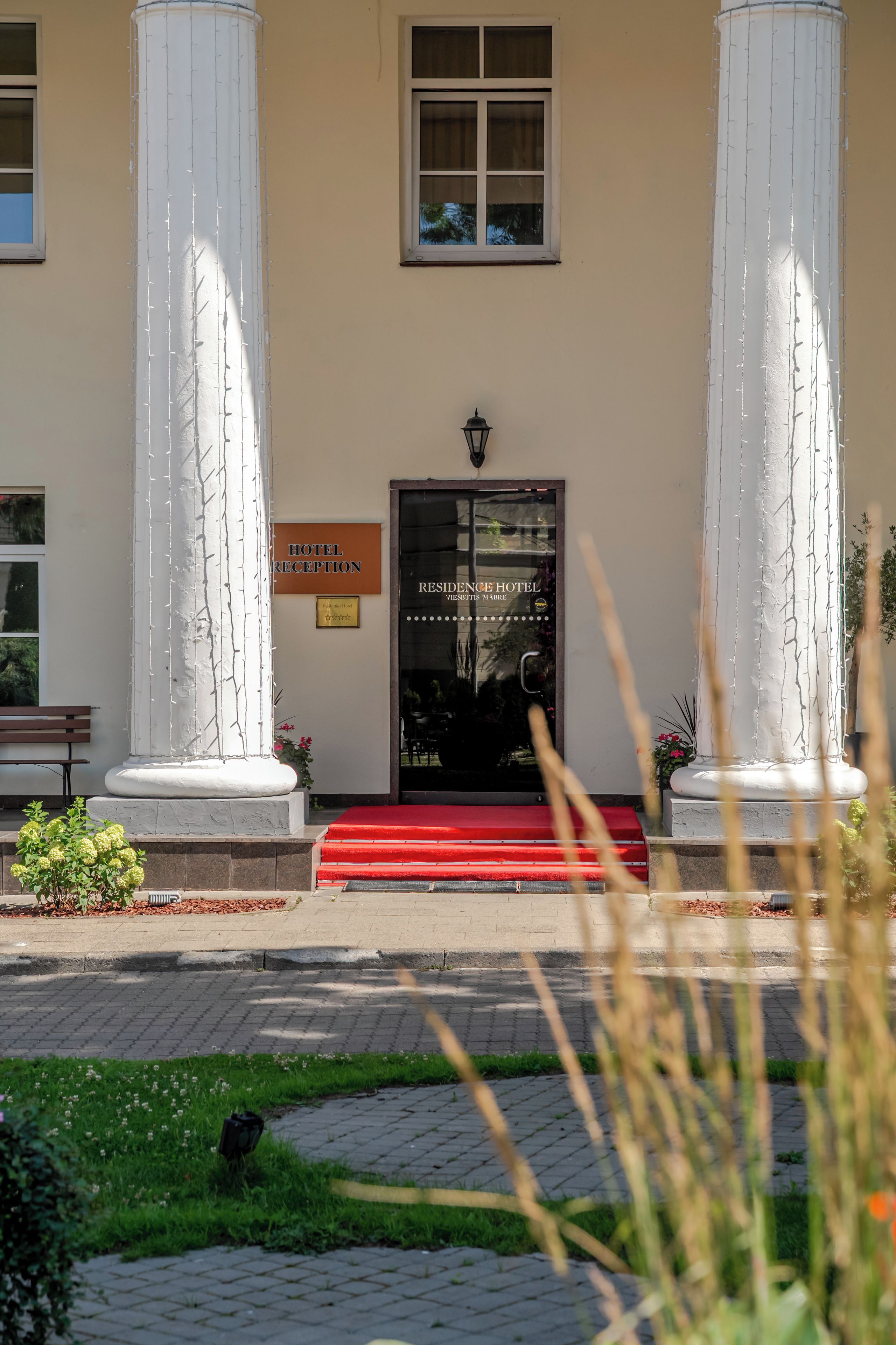 A hotel entrance with a reception sign, a red carpet, and two large columns.
