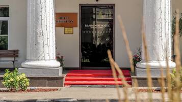 A hotel entrance with a reception sign, a red carpet, and two large columns.