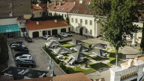A courtyard with outdoor seating, parked cars, and a building with a tiled roof. - Mabre Residence Hotel (Vilnius)