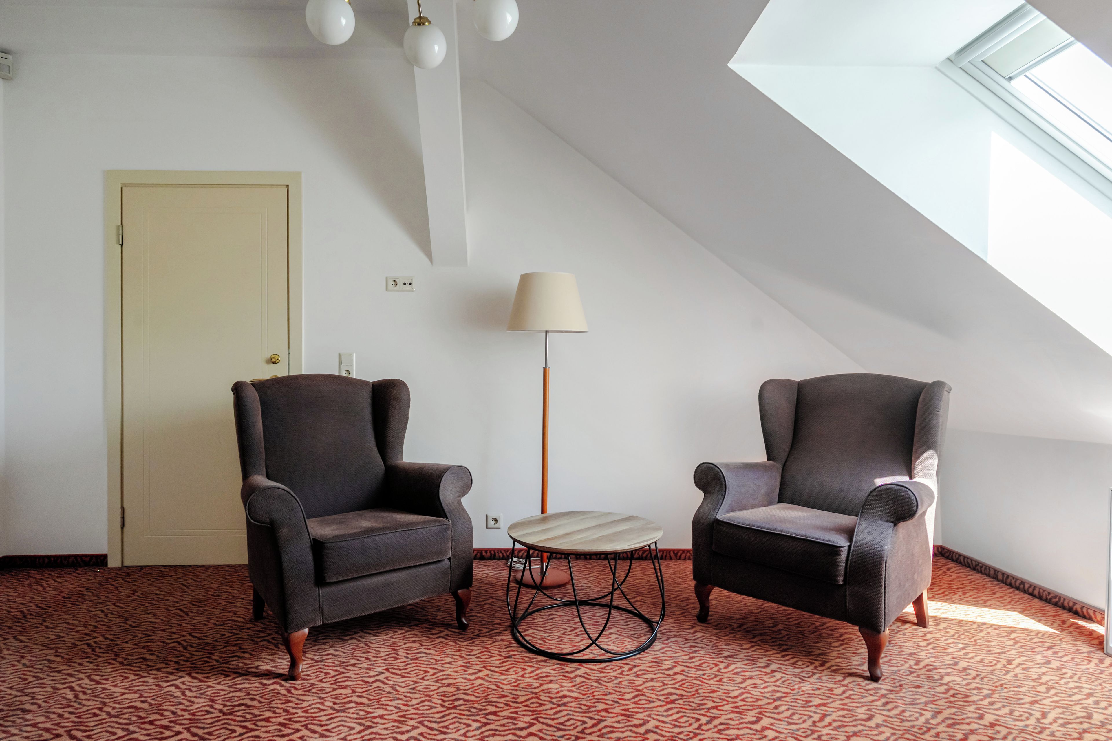 Ein Zimmer mit zwei Sesseln, einem kleinen runden Tisch, einer Stehlampe und einer Tür.
