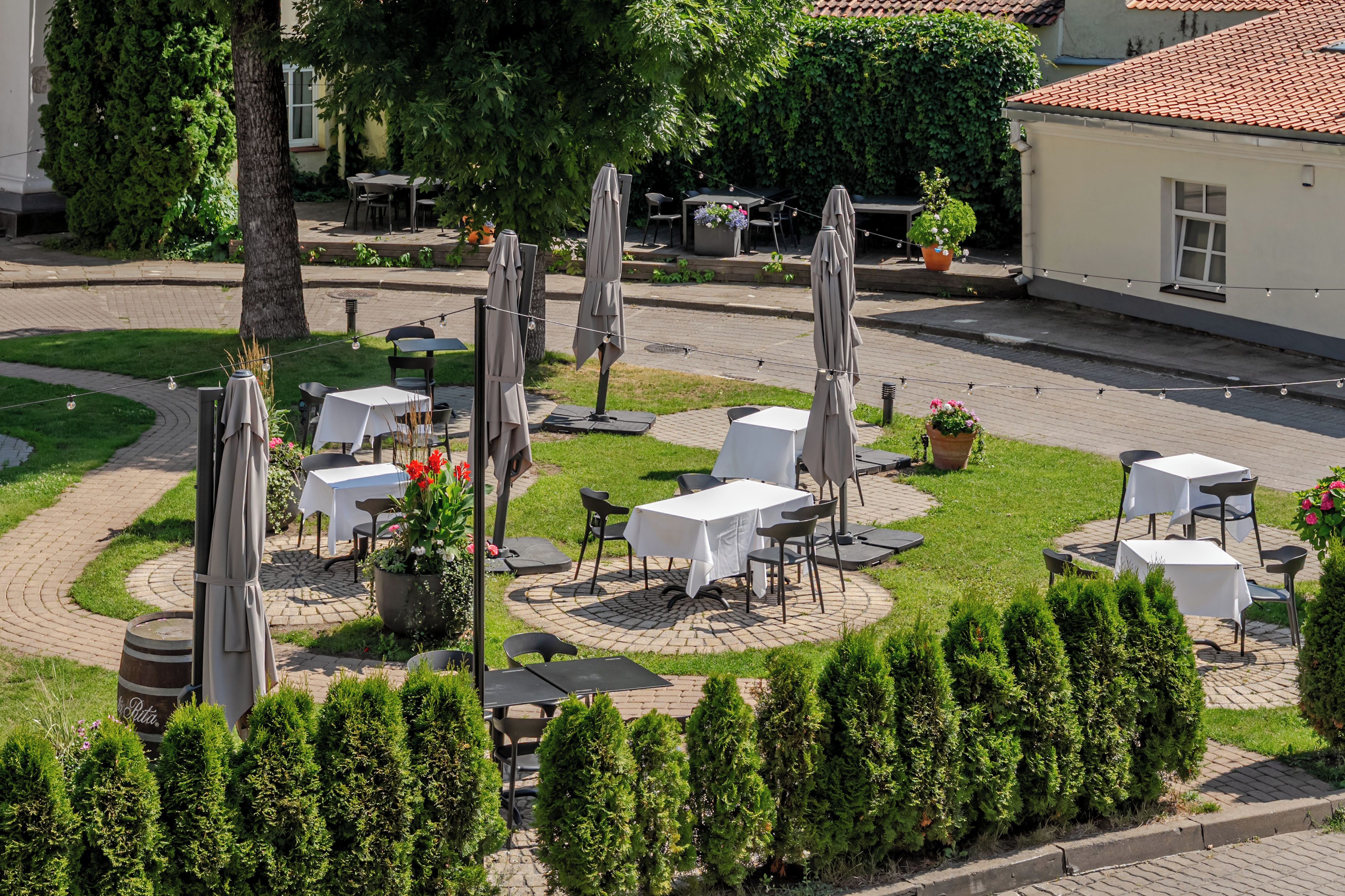 Un espace extérieur aménagé avec des tables et des chaises disposées en cercle, entouré de verdure et bordé d’un chemin pavé.