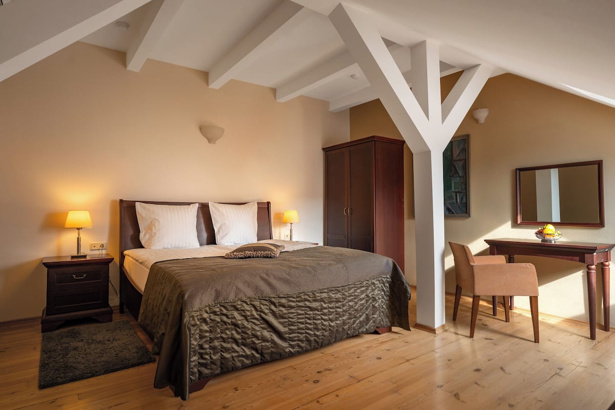 A bedroom with a large bed, two bedside tables with lamps, a wooden desk, a chair, and a wardrobe.