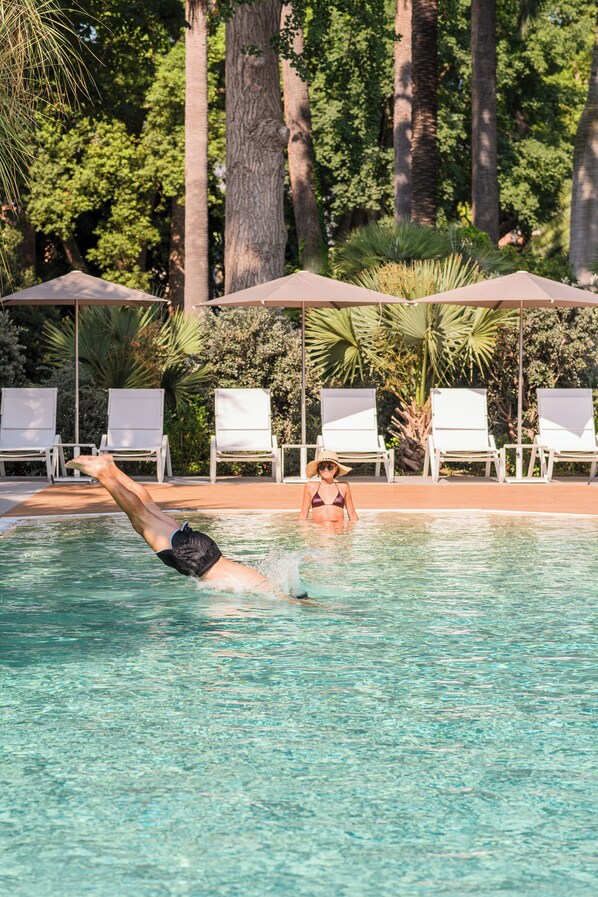 A swimming pool with clear water, surrounded by white lounge chairs and umbrellas. - So' Lifestyle Hotel Sorrento (Sorrento)