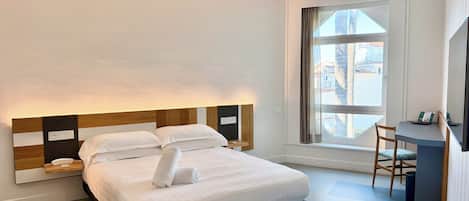 A modern hotel room with a large bed, bedside tables, a desk, and a window with a view.