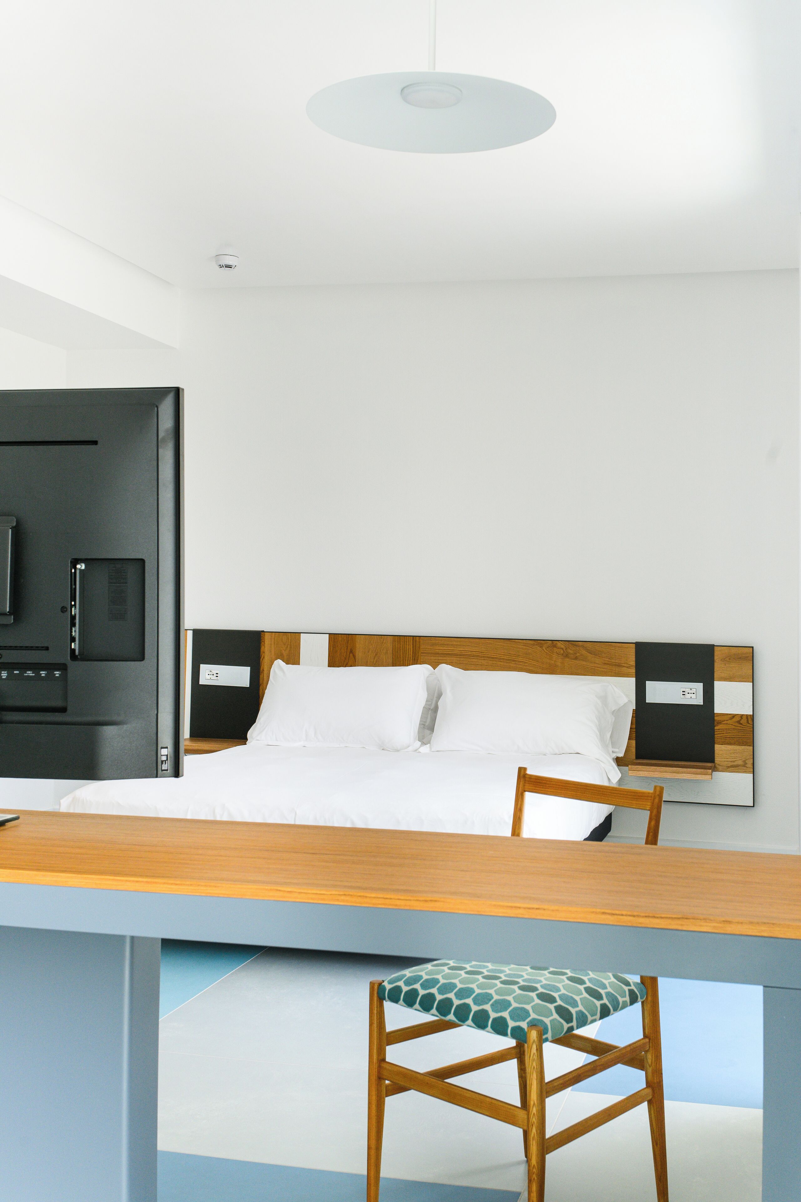A modern hotel room with a bed, a desk, and a chair.