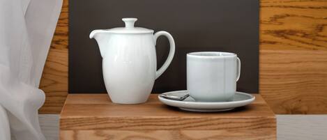 A modern room with a wooden bedside table, a white kettle, and a cup on a saucer.
