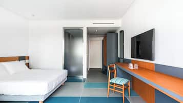 A hotel room with a bed, a desk with a chair, a television, and a door leading to another room.