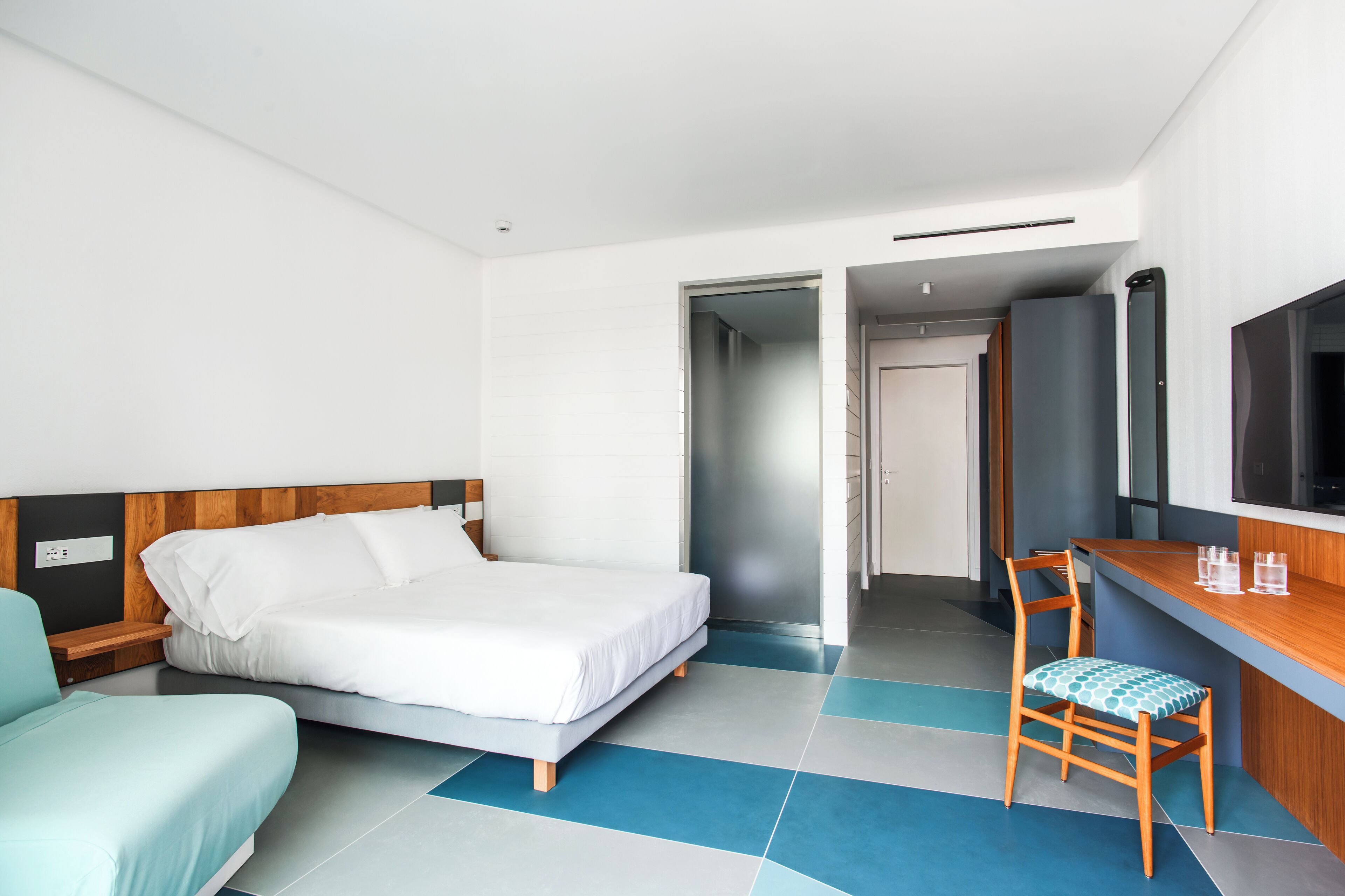A modern hotel room with a bed, a desk, a chair, and a television.