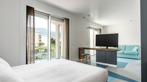Una habitación de hotel moderna con una cama grande, televisión, sofá y balcón con vistas a la ciudad.