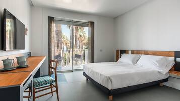 A modern hotel room with a bed, a desk with a chair, a television, and a balcony with a view of palm trees.