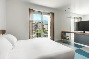A hotel room with a large bed, a desk with a chair, a television, and a balcony with a view of buildings and greenery. - So' Lifestyle Hotel Sorrento (Sorrento)