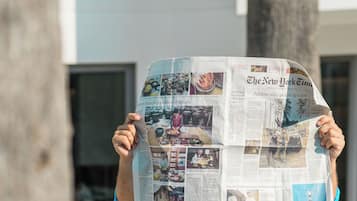 Eine Person hält eine Zeitung mit verschiedenen Artikeln und Bildern.