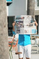 Eine Person hält eine Zeitung mit verschiedenen Artikeln und Bildern.
