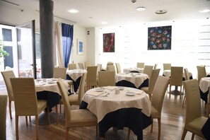 A restaurant with round tables and chairs, white tablecloths, and artwork on the walls. - Duca D'aosta (Mogliano Veneto)