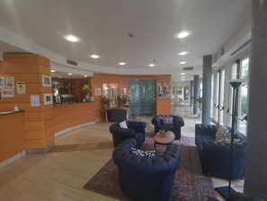 A lobby with a reception desk, seating area, and large windows. - Duca D'aosta (Mogliano Veneto)