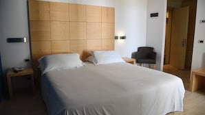 A hotel room with a large bed, a wooden headboard, bedside tables, a chair, and a wardrobe.