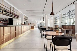 A modern bar area with a long counter, shelves of bottles, and hanging glasses. There are tables and chairs arranged for seating. - Best Western Hotel Tranas Statt (Tranas)