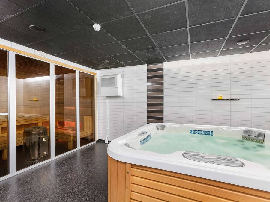 Uma área de spa moderna com hidromassagem, bancos de madeira e divisória de vidro.