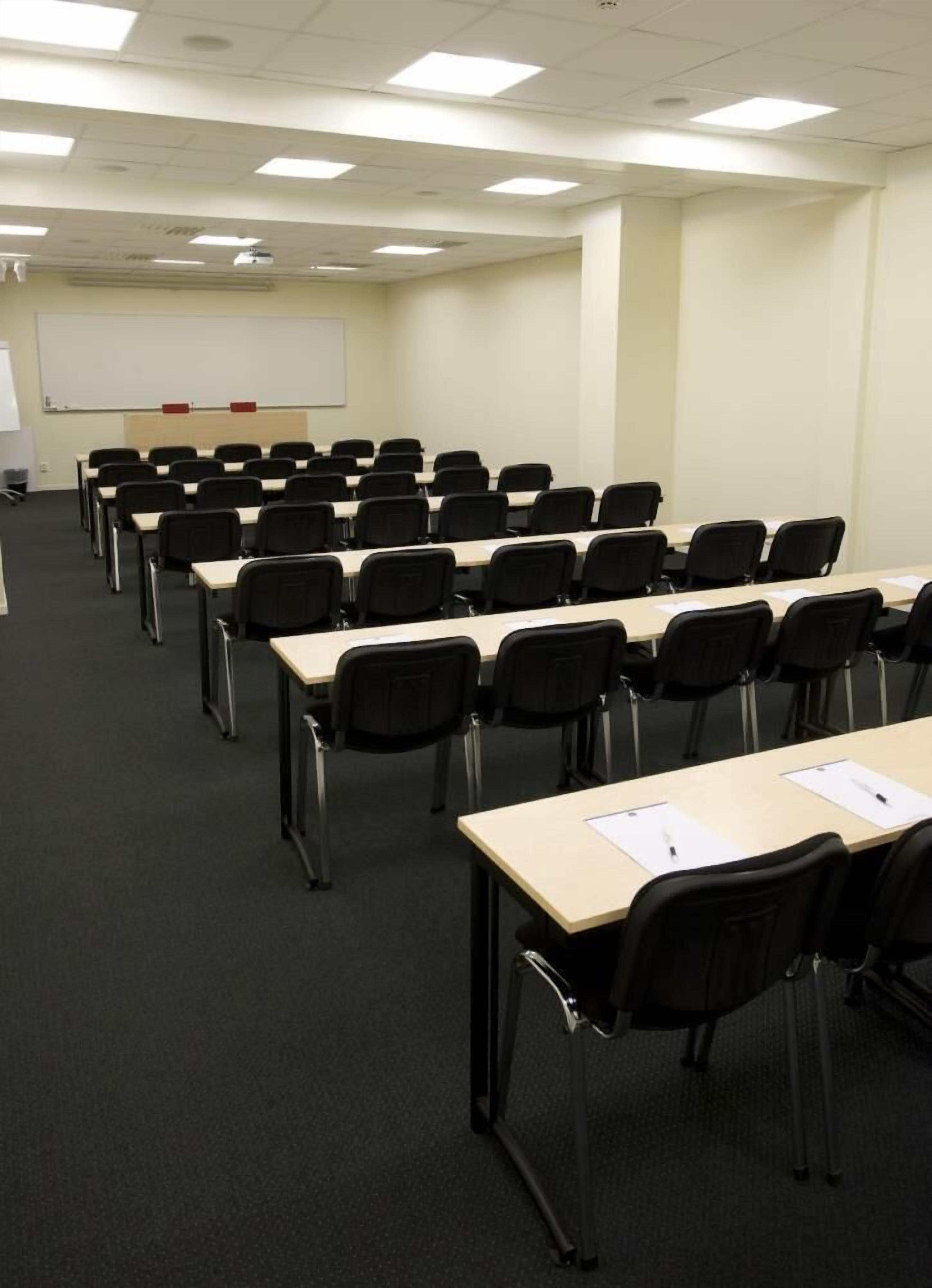 A conference room with rows of tables and chairs, a whiteboard, and a projector screen.