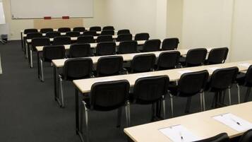 A conference room with rows of tables and chairs, a whiteboard, and a projector screen.