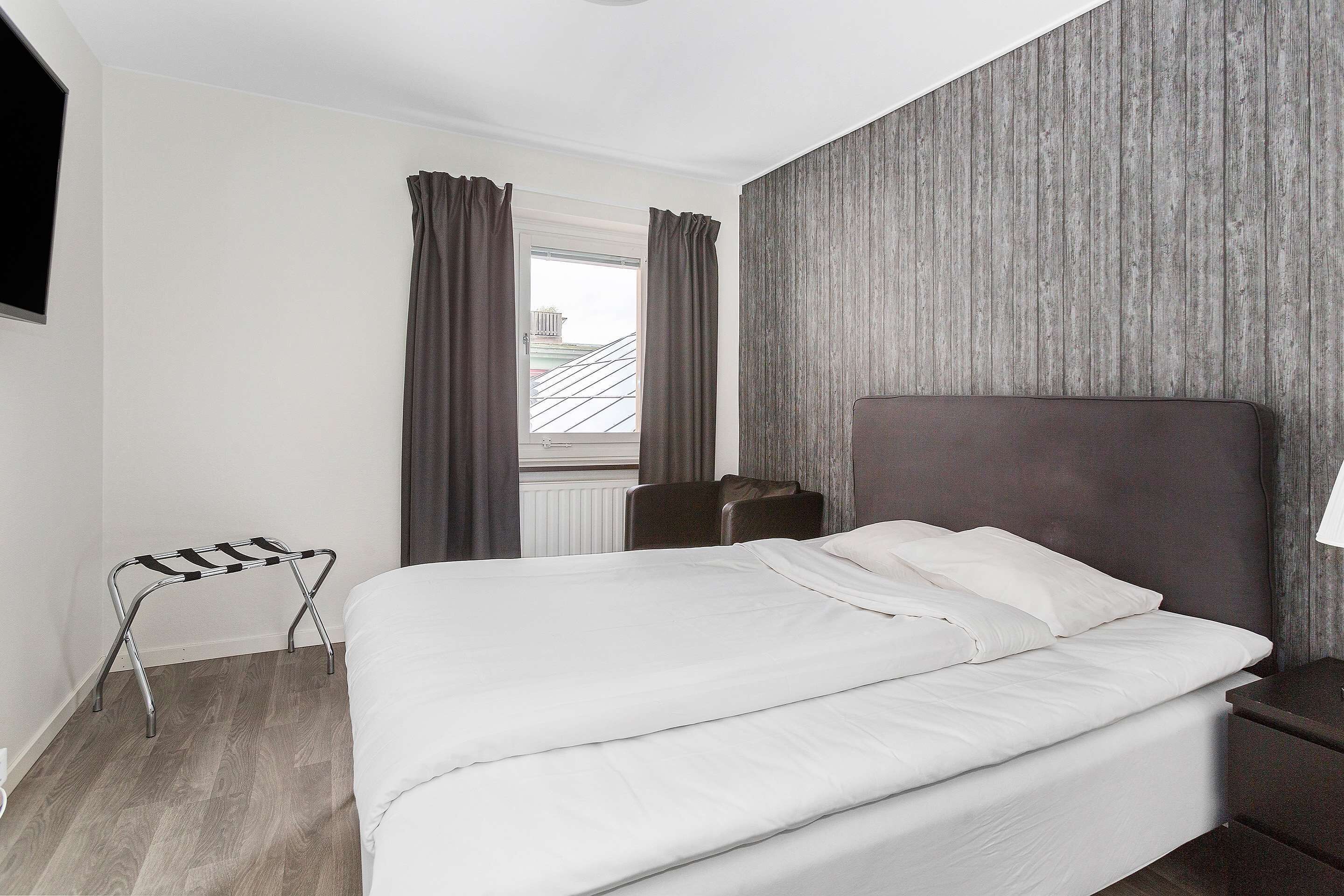 En pænt redt seng på et hotelværelse med sengegavl i træ, et lille bord og en stol.
