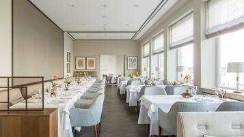 Un comedor espacioso con largas mesas dispuestas para varios invitados, amplias ventanas que ofrecen luz natural y obras de arte enmarcadas en las paredes.