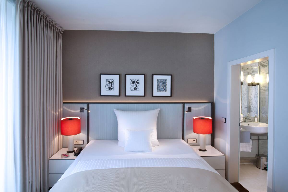 Une chambre d’hôtel avec un lit, deux lampes de chevet, une table de nuit, une tête de lit et trois tableaux encadrés accrochés au mur.
