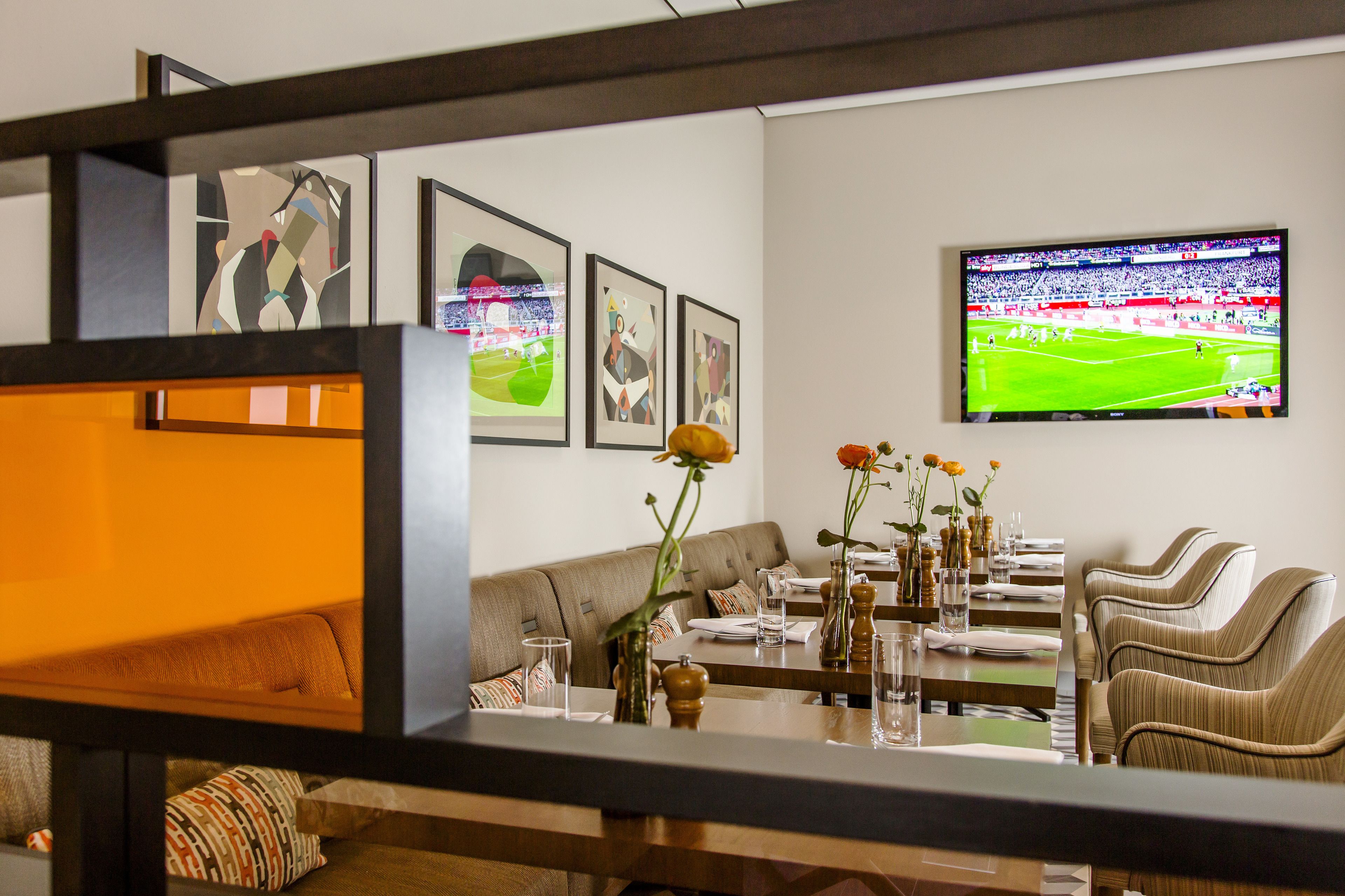 A dining area with a television displaying a soccer match, a sofa, and a table set with glasses and flowers.