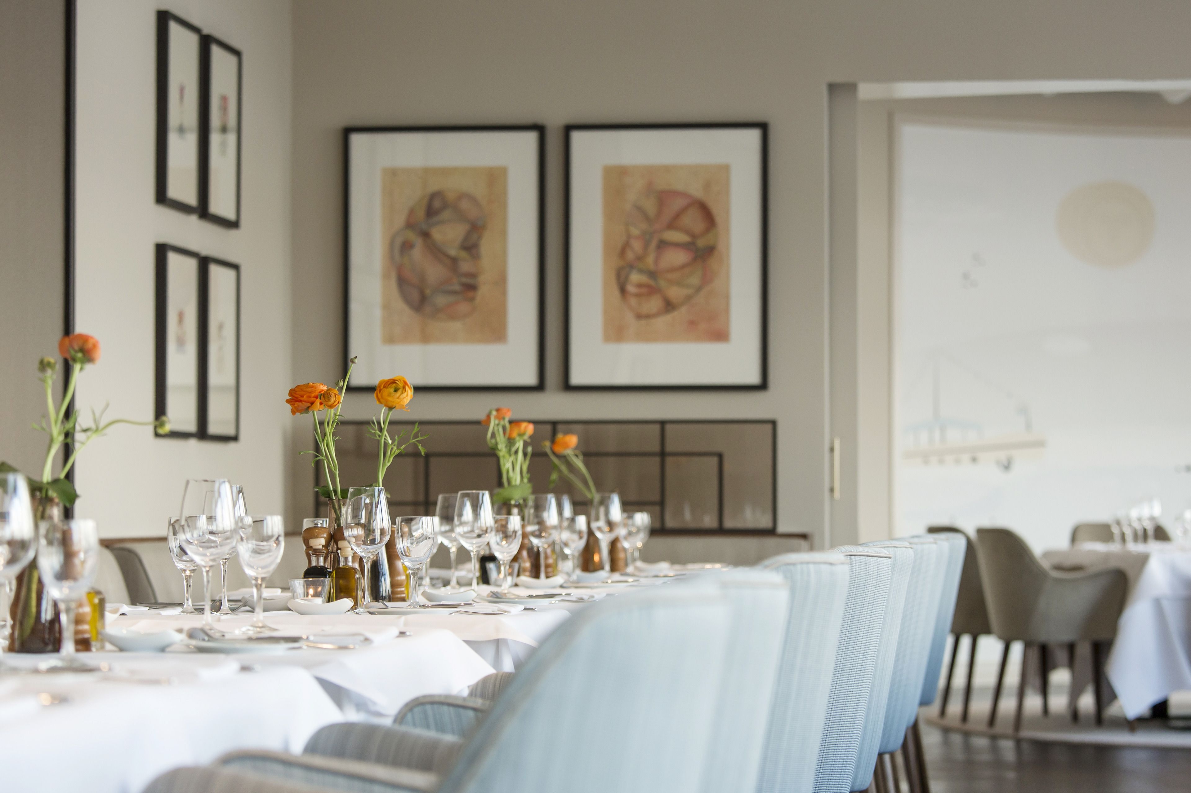 Un comedor con una mesa larga dispuesta para una comida, una obra de arte enmarcada en la pared y vista del cuarto.