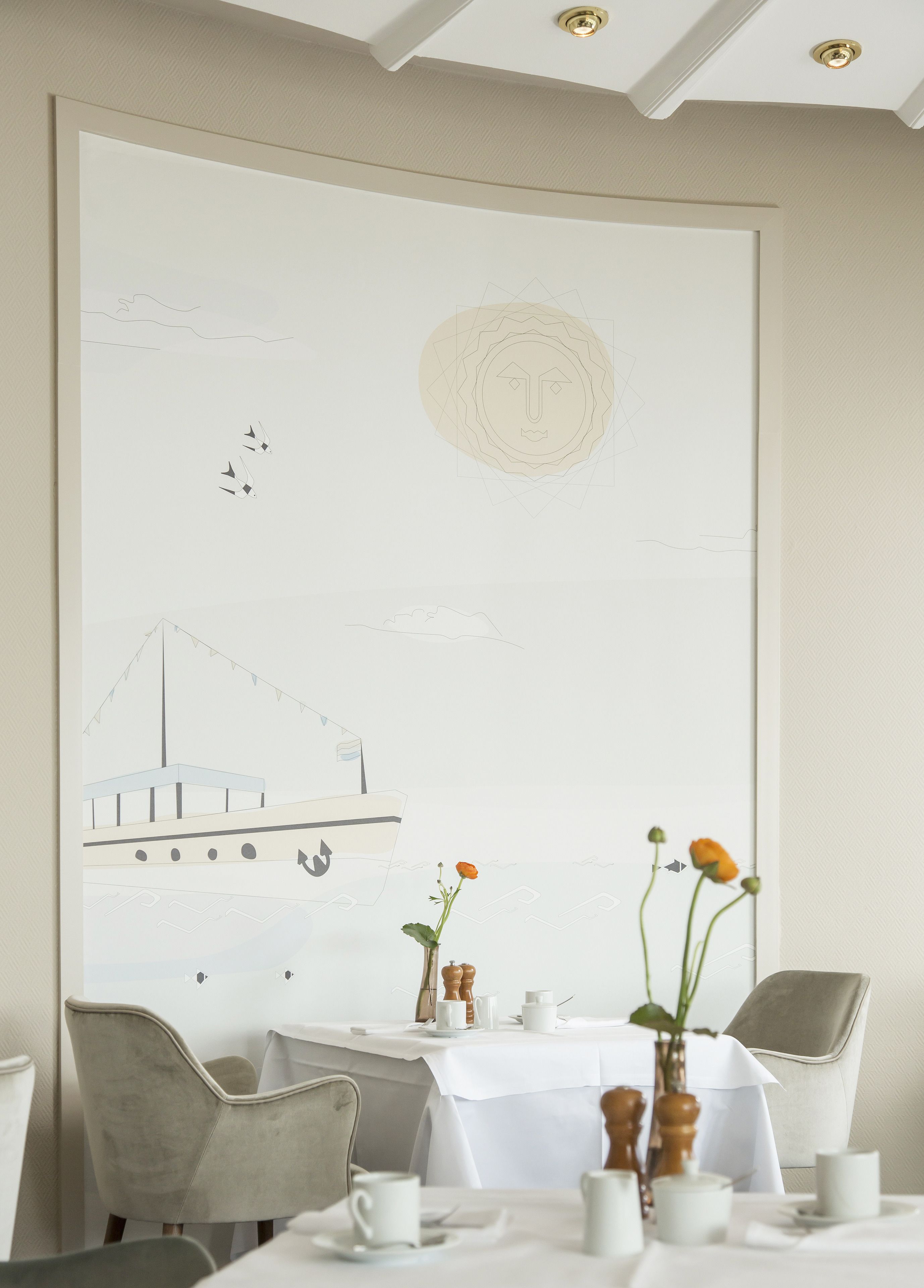 Un coin repas avec une table dressée pour deux personnes, une grande peinture abstraite au mur et une vue sur la mer.