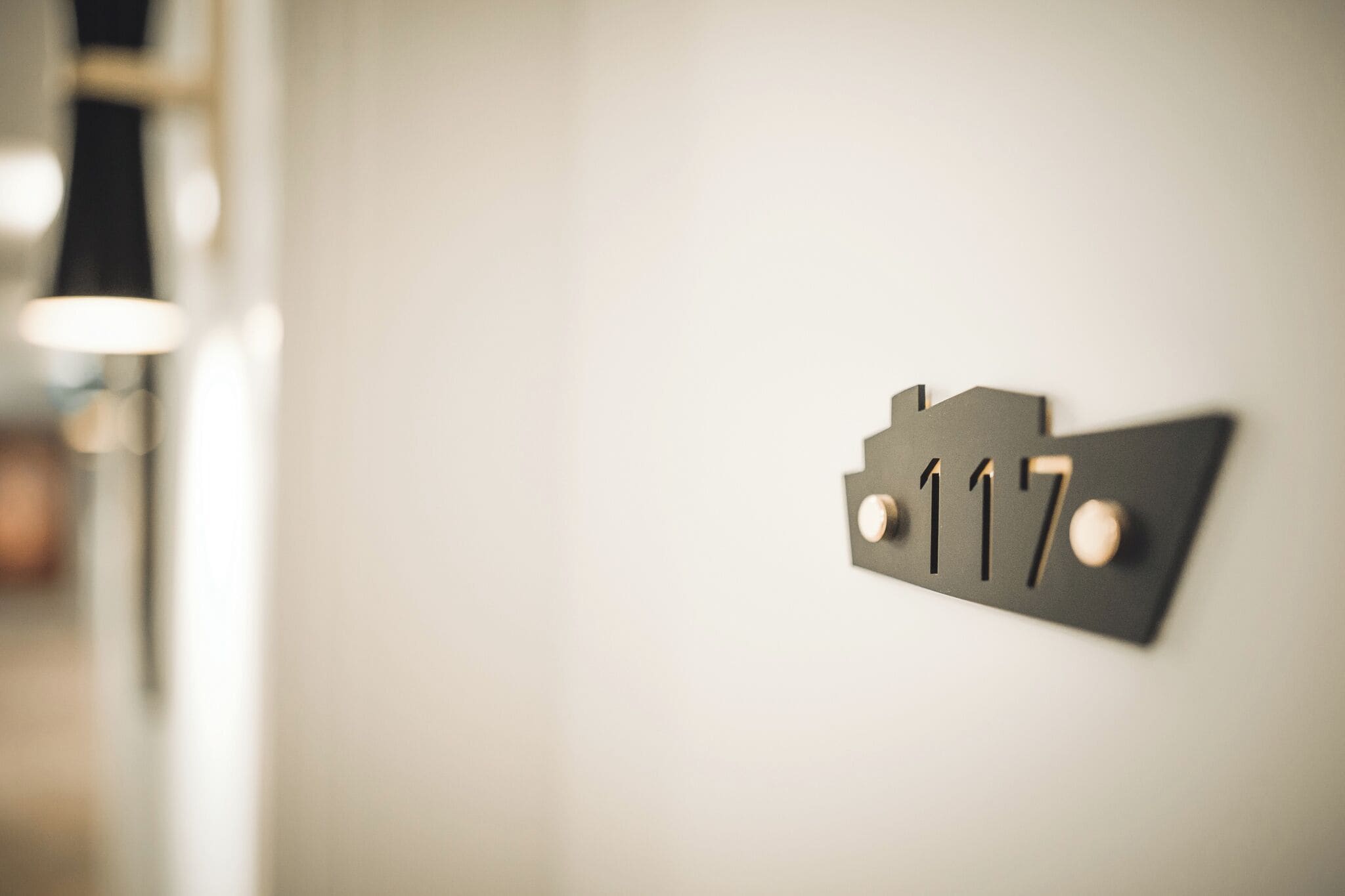 A close-up of a black metal sign with the number 117 on a white wall.