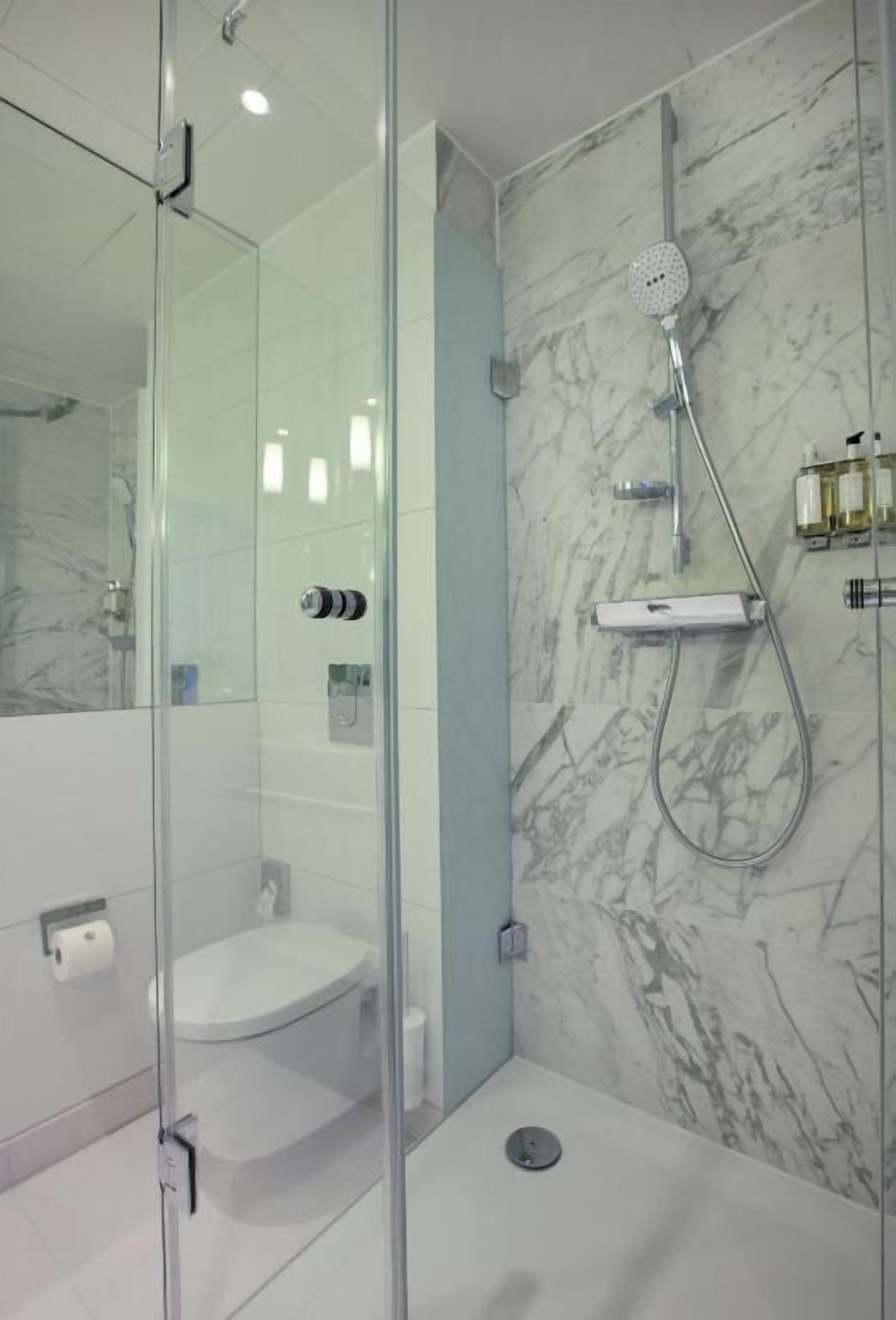 A modern bathroom with a glass-enclosed shower, a marble wall, and a toilet.