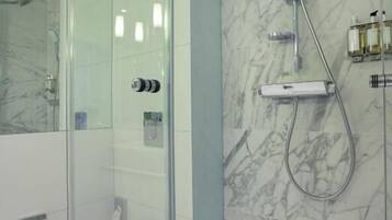 A modern bathroom with a glass-enclosed shower, a marble wall, and a toilet.