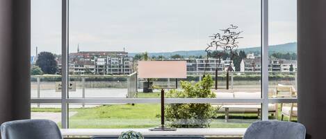 Una habitación moderna con dos sillones grises, una pequeña mesa redonda y vistas a un paisaje urbano a través de amplios ventanales.