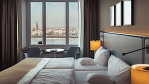 Une chambre d’hôtel dotée d’une grande fenêtre donnant sur la ville, d’un lit, d’un bureau et d’une chaise.