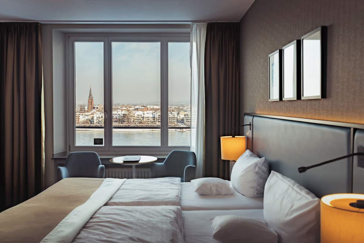 Une chambre d’hôtel dotée d’une grande fenêtre donnant sur la ville, d’un lit, d’un bureau et d’une chaise.