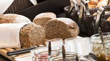 Variedad de panes y pasteles expuestos en cestas y sobre una tabla de madera, con frascos de vidrio y utensilios cerca.