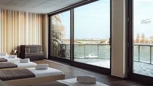 Une chambre d’hôtel moderne avec de grandes fenêtres, une vue sur une rivière et un lit avec une valise.