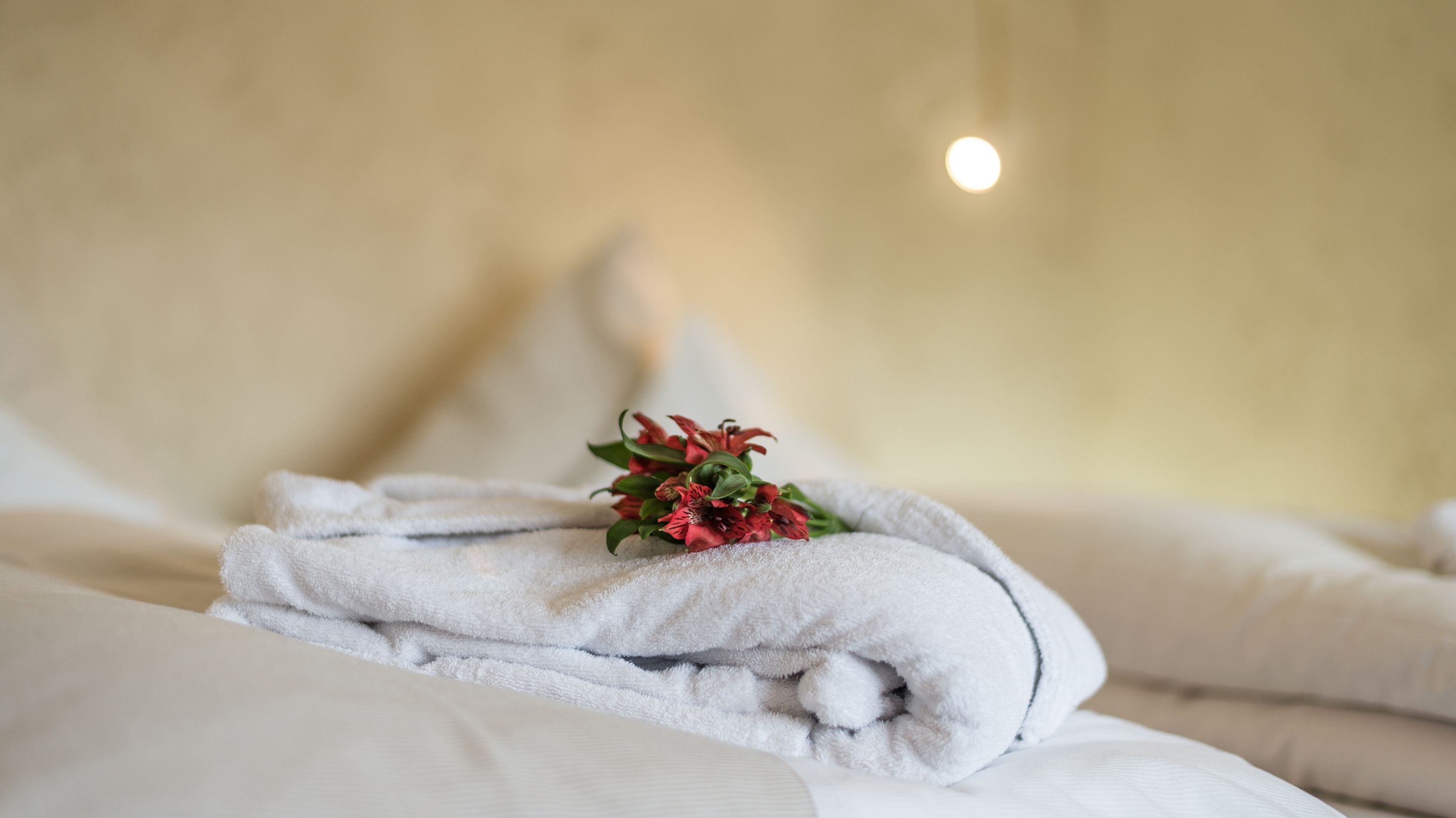 Ein ordentlich gemachtes Bett mit weißen Leinen und einem kleinen Strauß roter Blumen darauf.