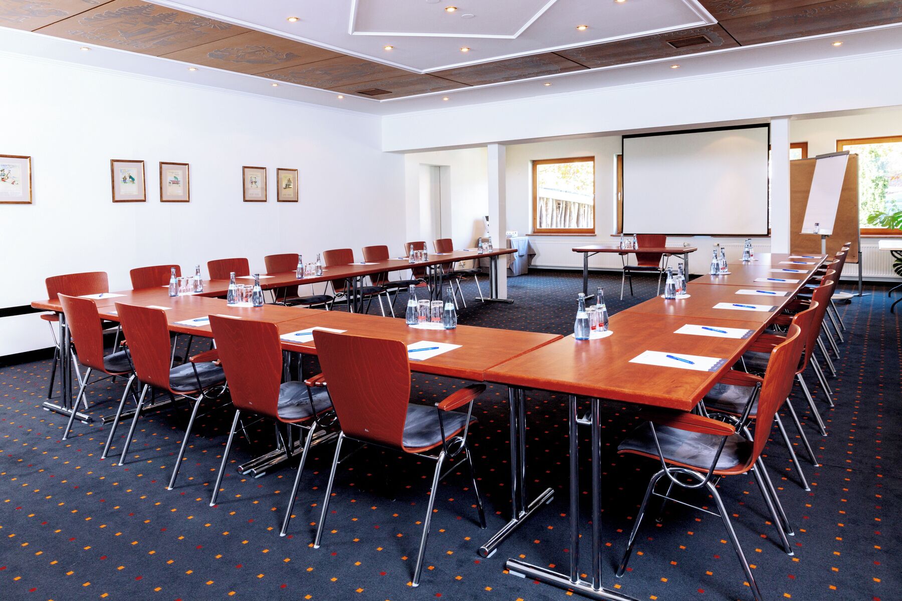 A conference room with long tables, chairs, and a projector screen.