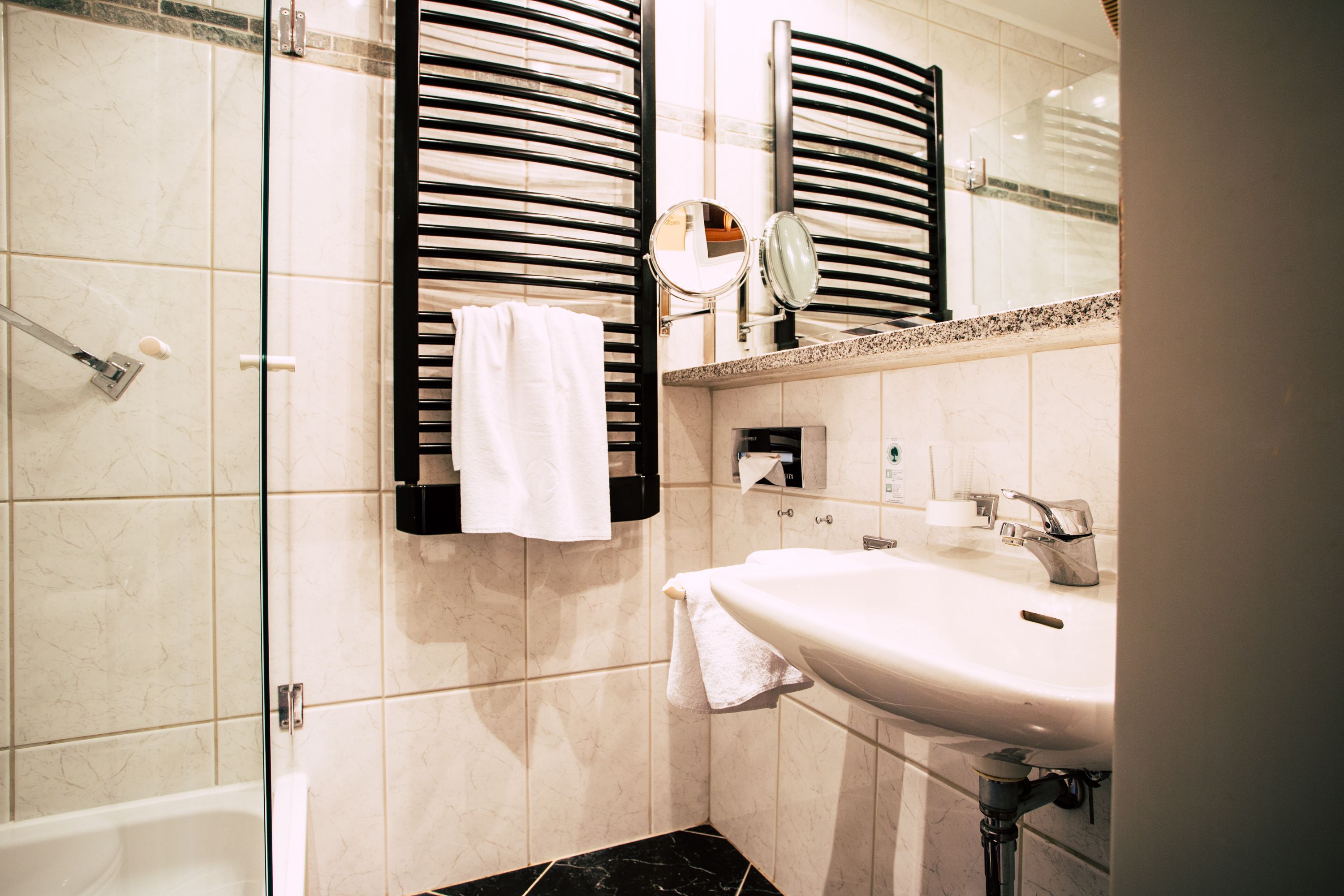 Un baño con ducha envuelta en vidrio, un lavamanos blanco y un espejo encima.