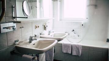 A bathroom with two sinks, a mirror, a window, and a bathtub.