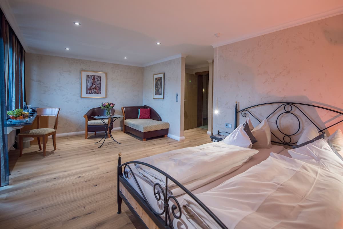 A hotel room with a bed, a sofa, a dining table with chairs, and a small table with a vase of flowers.
