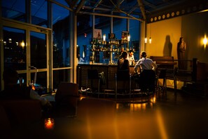 Un espace bar doté d’un haut plafond, de grandes fenêtres et offrant une vue sur la ville la nuit.