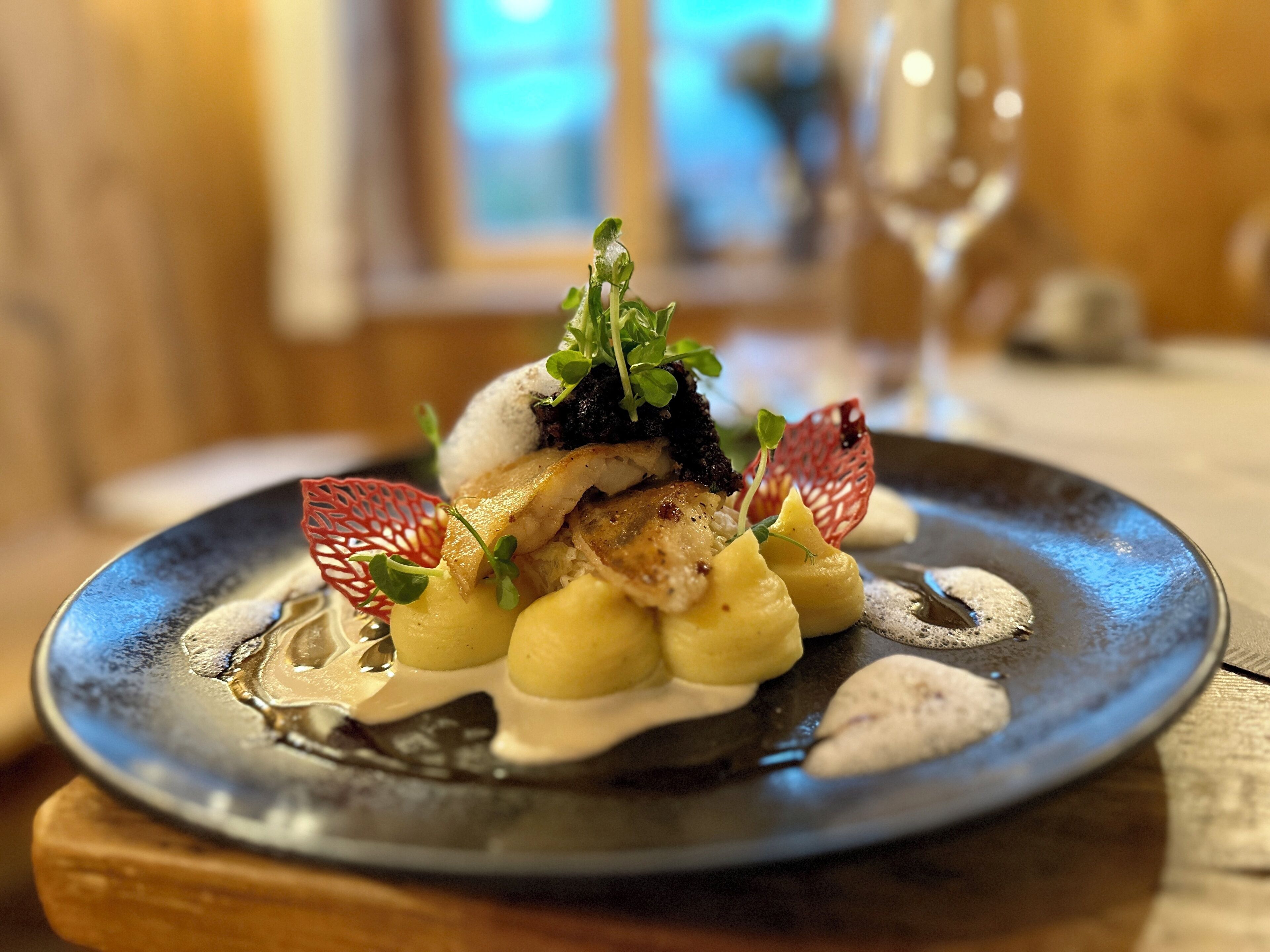 Ein Teller mit Fischfilet, Kartoffeln und Grünzeug, serviert auf einem dunklen Teller.