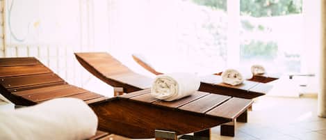 A spa room with wooden loungers, a towel, and a view of greenery outside.