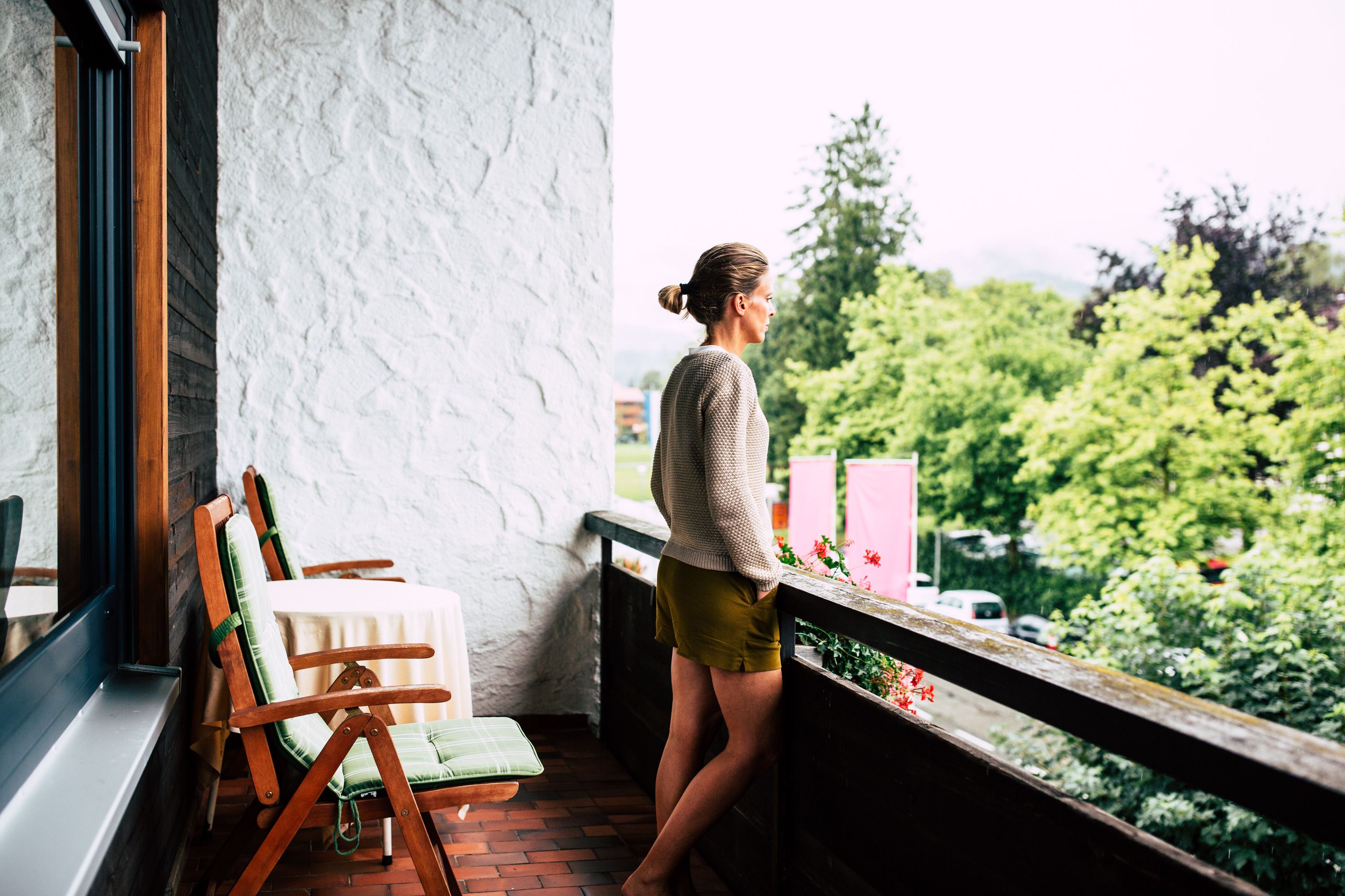 A balcony with a view of greenery, a wooden chair, and a table.