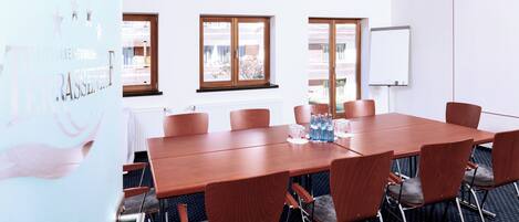 A conference room with a long table, six chairs, a whiteboard, and windows with a view of buildings outside.
